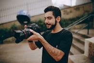 A young man focusing a DSLR camera outdoors, preparing for a photoshoot.